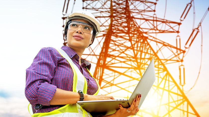 Woman worker checking information on a laptop while checking a large electrical tower