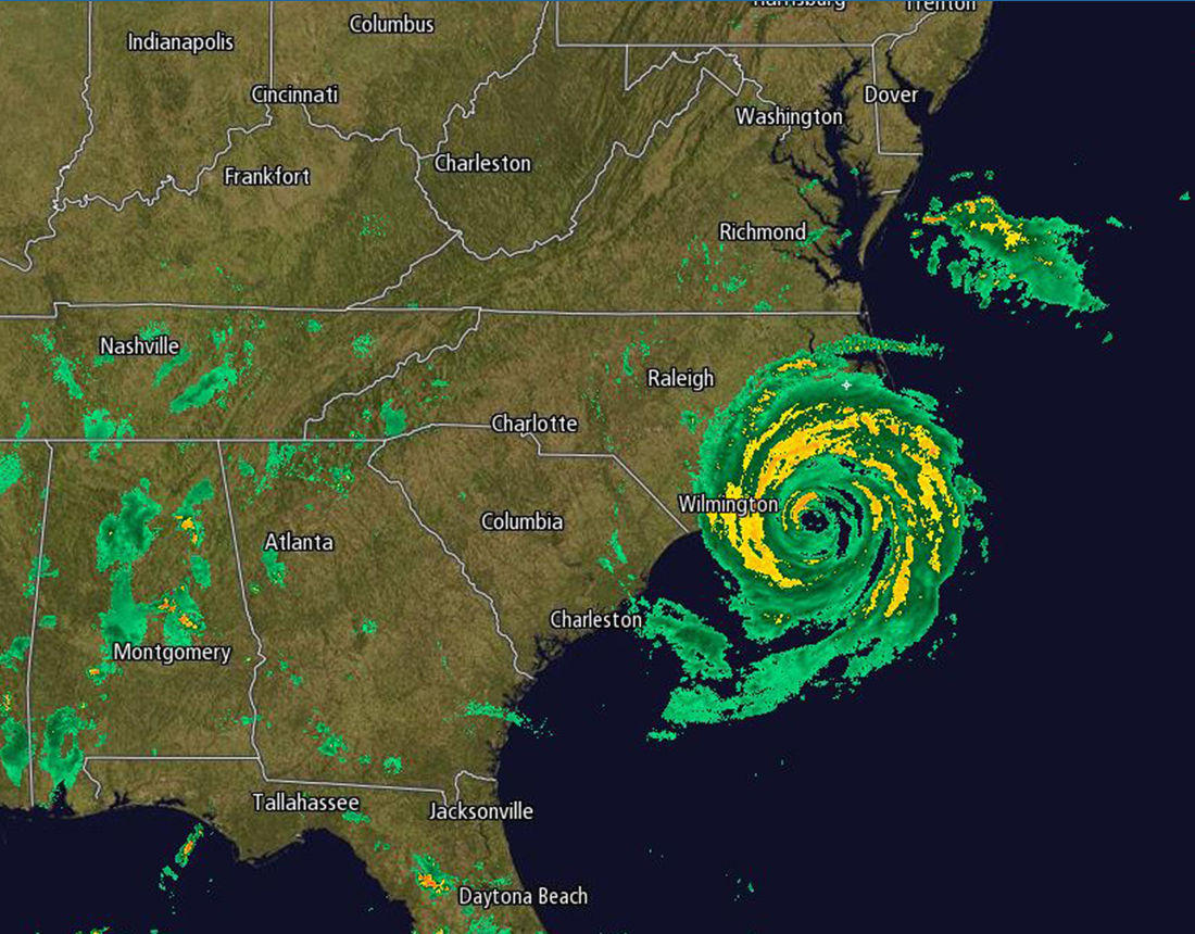 Satellite imagery shows a hurricane swirling near Wilmington, North Carolina, with distinct yellow and green bands indicating heavy rainfall.