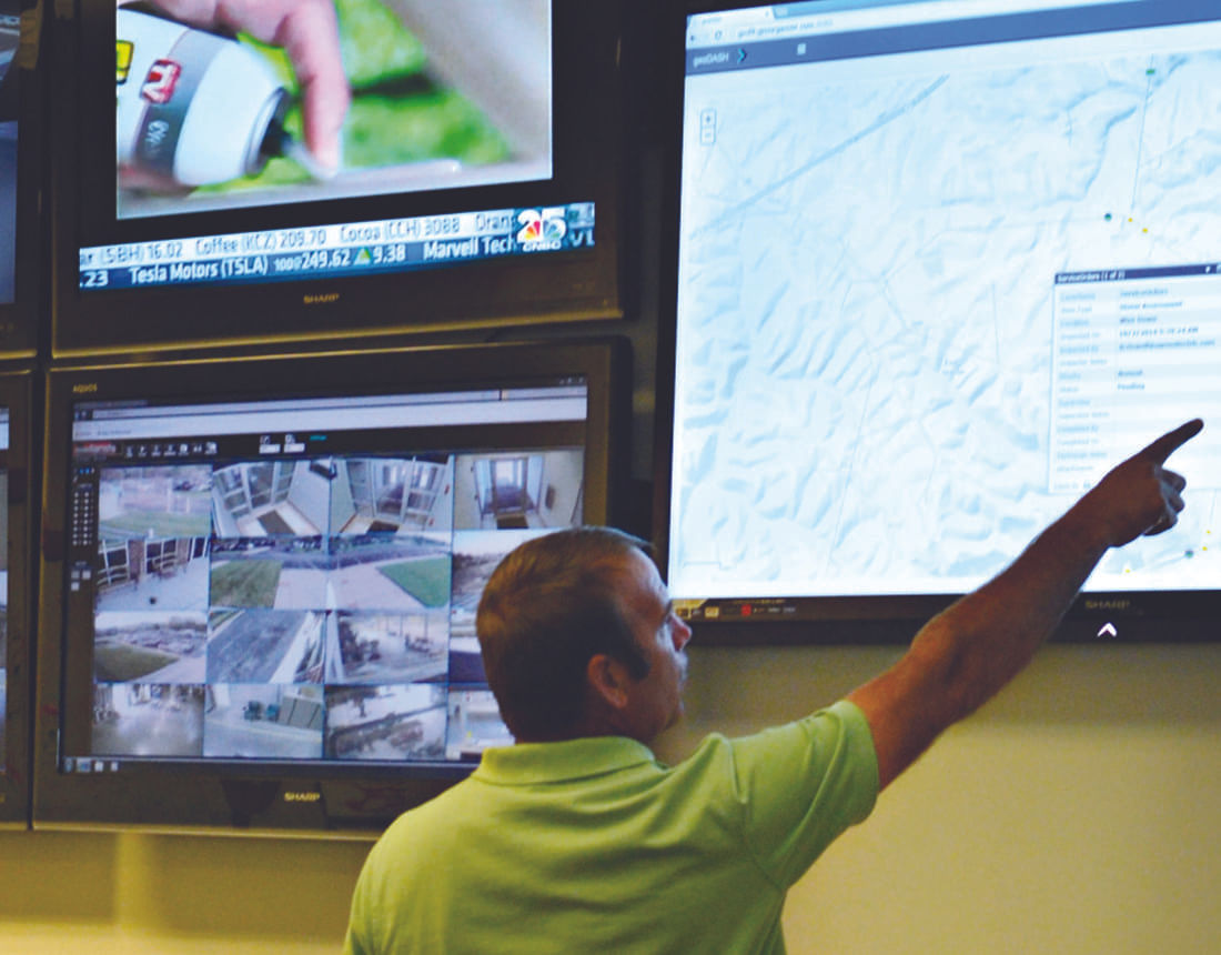 A man in a green shirt points at a large screen displaying a digital map interface.