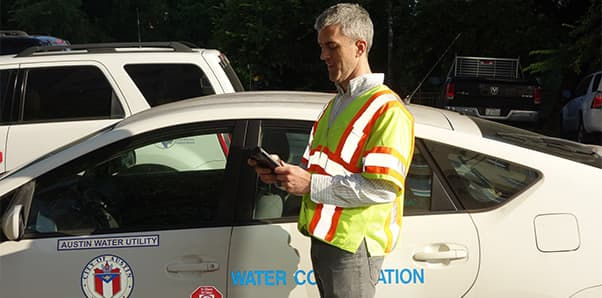 A utility worker wearing a high-visibility safety vest stands next to a marked Austin Water Utility vehicle. 