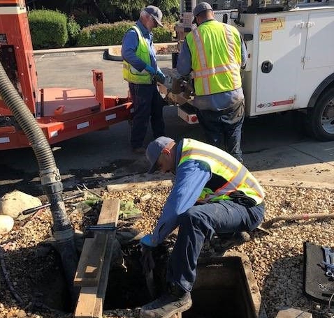Three utility workers in high-visibility vests are repairing underground infrastructure in a residential area. 
