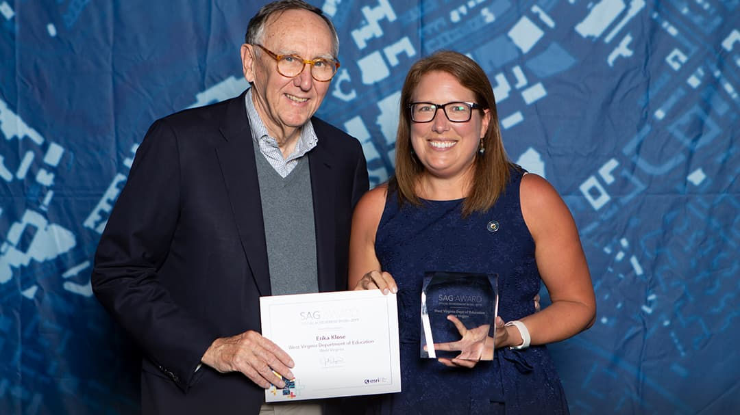 Two individuals are pictured at an award ceremony, holding a certificate and a glass trophy. 