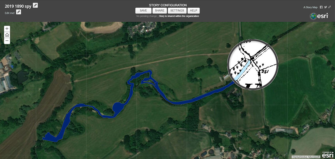 An aerial view showcasing a rural landscape with fields and greenery. A winding waterway is highlighted in blue, drawing attention to its path through the terrain.