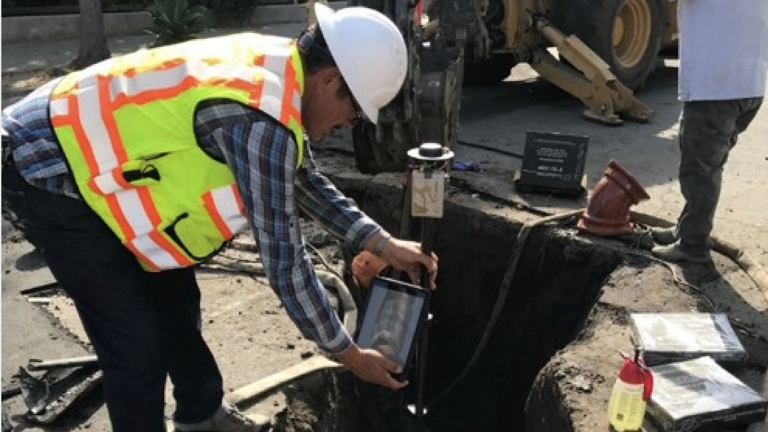 A construction worker wearing a safety vest and helmet is inspecting an underground utility site. 
