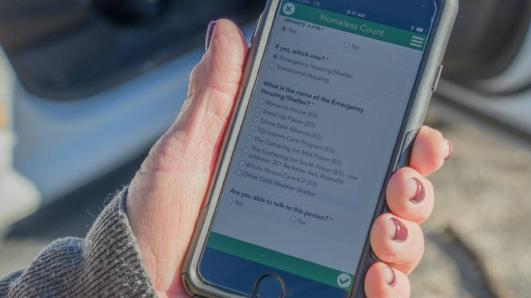 A close-up of a hand holding a smartphone displaying a survey application titled 'Homeless Count'.