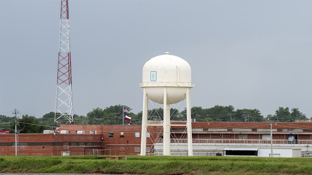 A large white water tower stands prominently in front of a red-brick industrial facility.