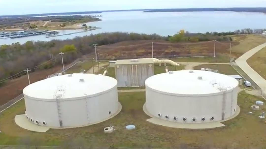 Two large cylindrical water storage tanks are situated in an open area near a lake.