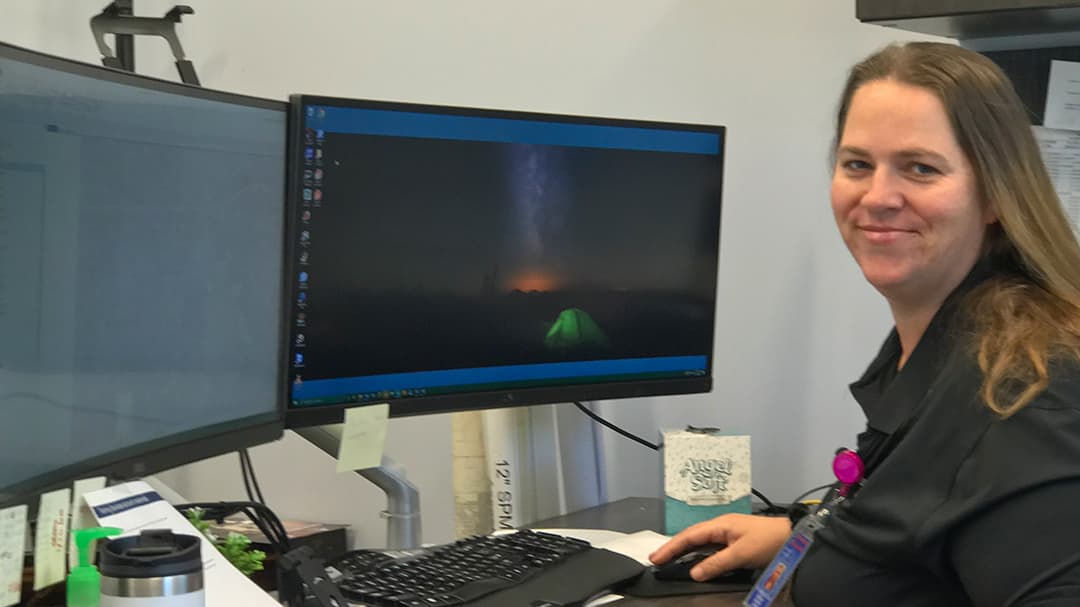 A workspace featuring dual monitors, one displaying a night sky with a glowing tent and horizon.
