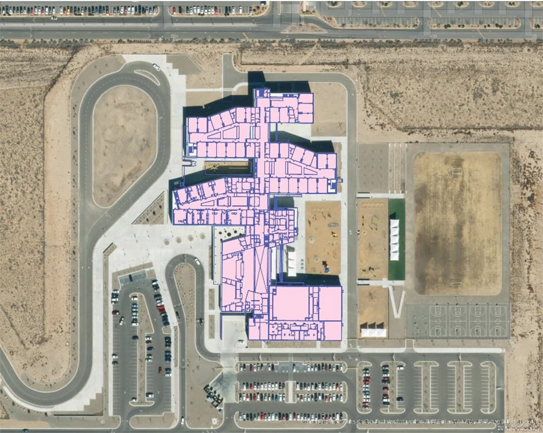 An aerial image showcasing a building layout highlighted in pink overlay, surrounded by parking lots and roads. 