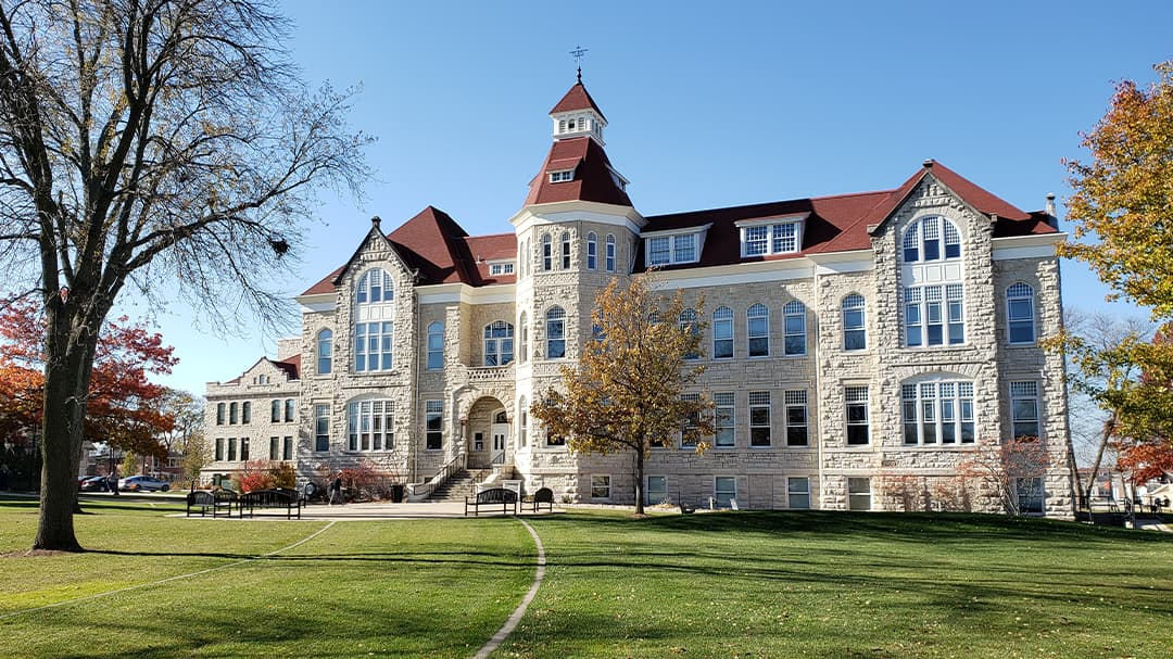 A large historic building constructed with light-colored stone and featuring a red roof and central tower. 