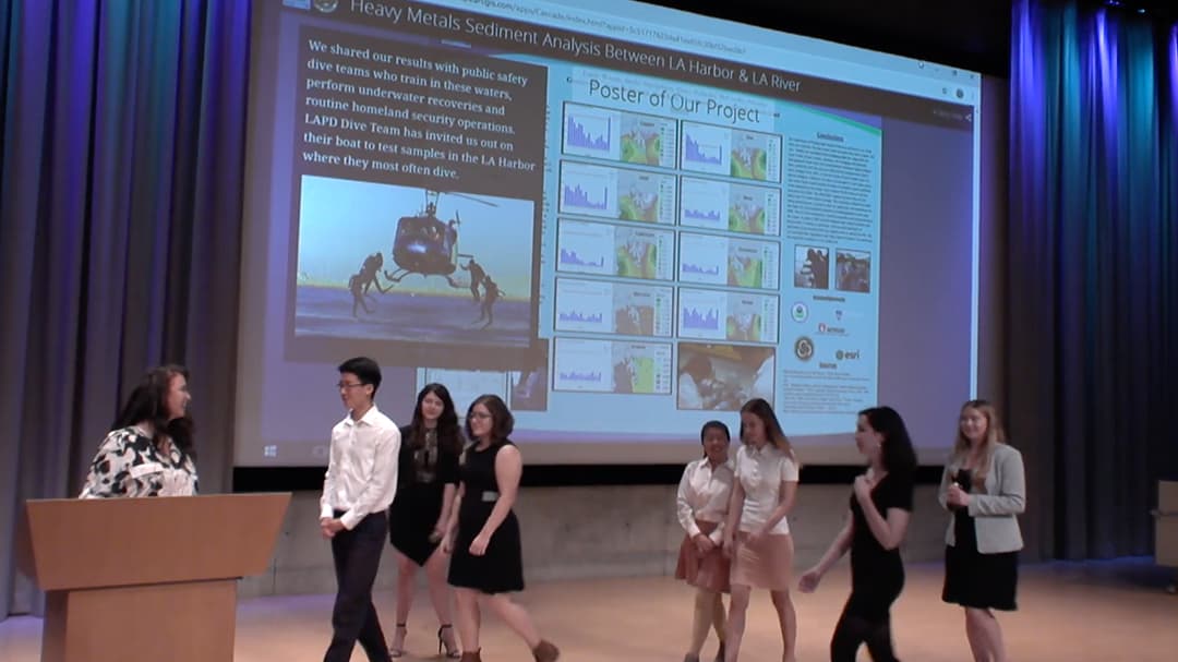 A diverse group of people is positioned in front of a screen, likely participating in a presentation or meeting.