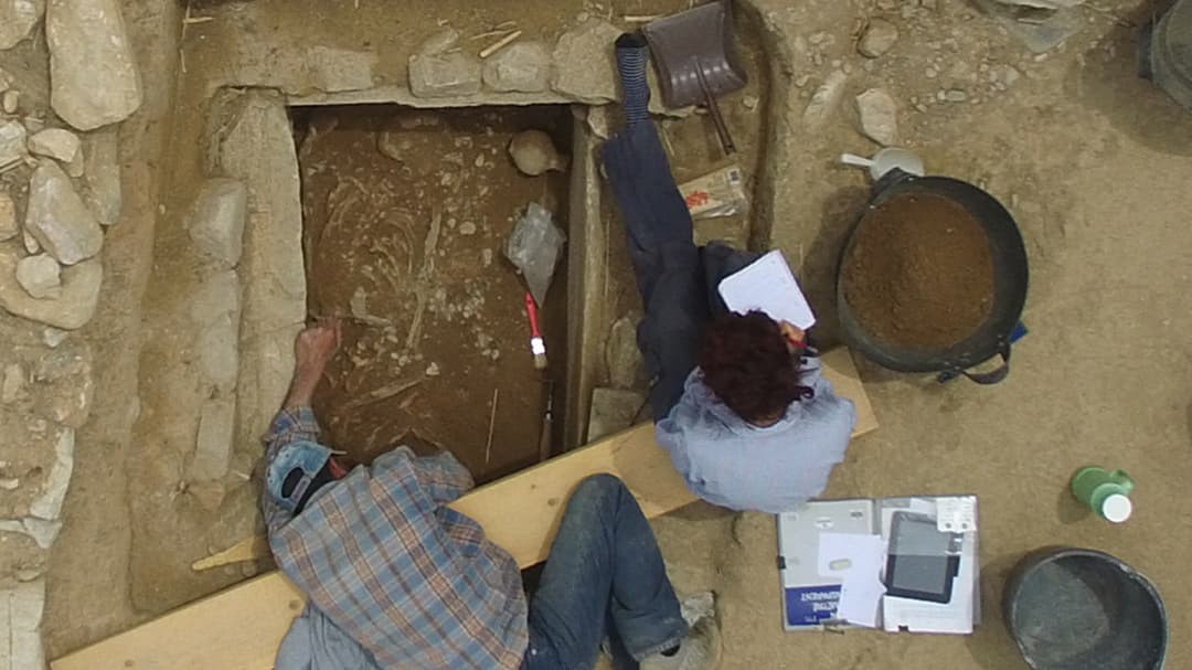 On overhead view of two archaeologists from NKUA uncovering and studying ancient artifacts in a rectangular hole