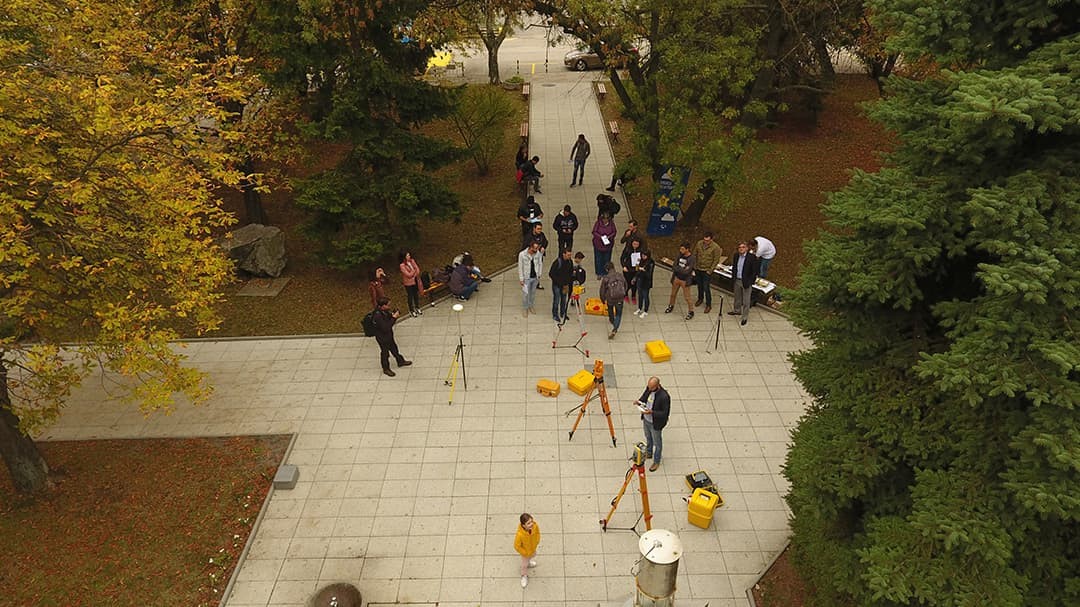 : A group of people on a paved walkway in a park using theodolites to take measurements