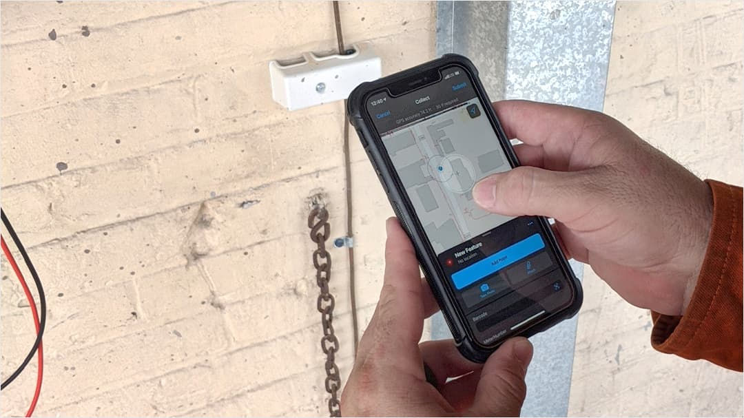 A close-up of hands holding a smartphone displaying a map-based application interface. 