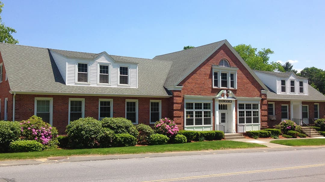 A red brick building featuring large windows and a symmetrical design, situated along a quiet street.