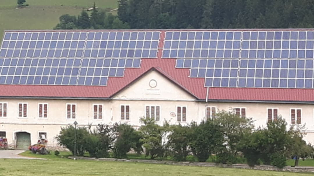 A large rural building with a red roof is covered with solar panels, showcasing renewable energy technology.