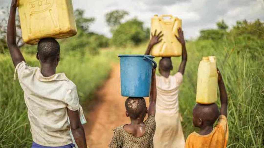 A group of young African children walk with buckets and jerrycans on their heads, bringing clean water back to their village.