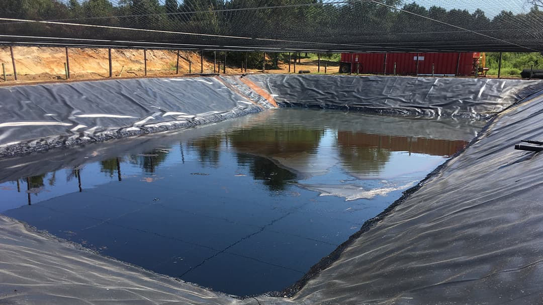 A large industrial water containment pond lined with black geomembrane material is shown.