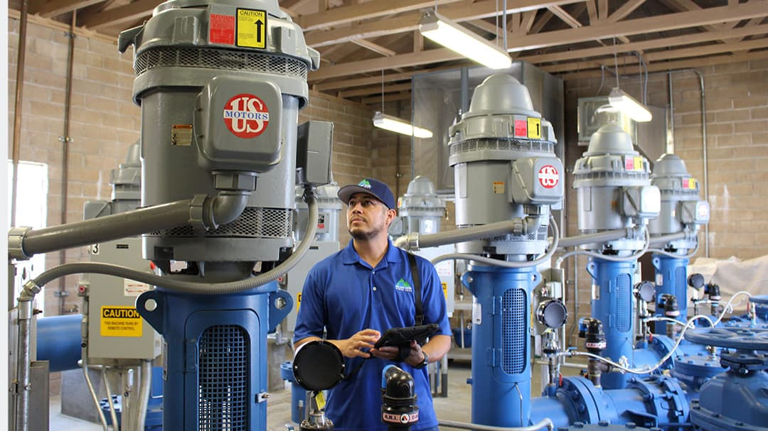 A row of large industrial machines labeled 'Roots' is displayed in a factory environment with exposed wooden beams and bright lighting. 