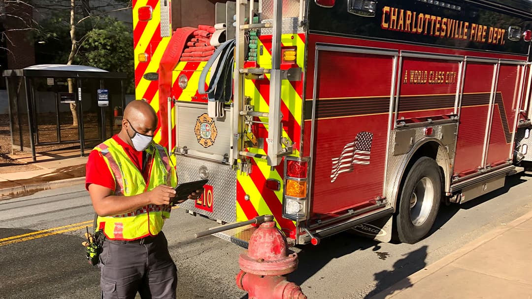 A firefighter in a high-visibility vest stands near a red fire truck labeled 'Charlottesville Fire Dept.' 