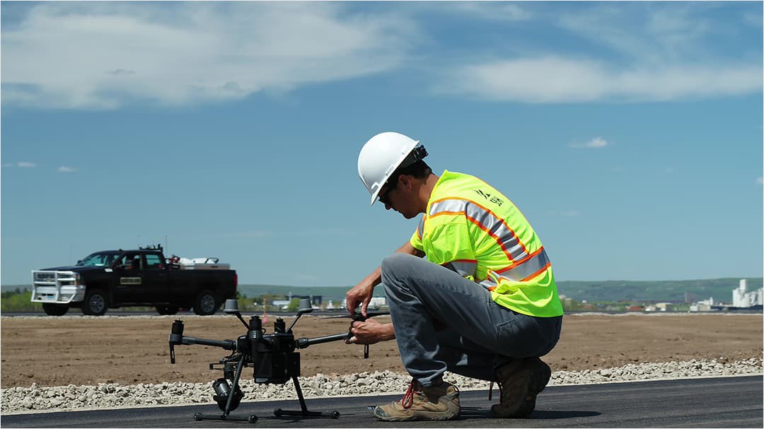 Drone pilot kneeling on pavement of a construction site, preparing his drone for takeoff