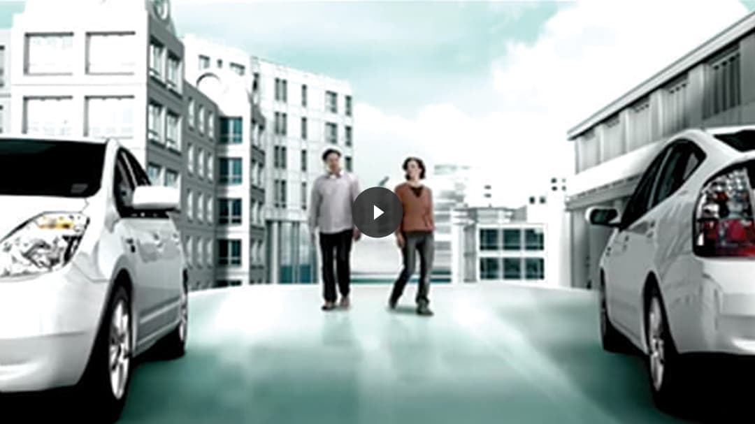 Two people walking between two Prius vehicles overlaid with video play thumbnail