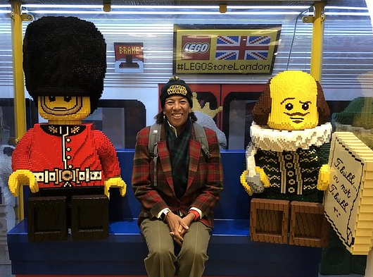 Dawn Wight sits in between two life-size sculptures made of LEGOS. The Sculpture on the right is a royal British guard and the sculpture on the left is Shaekspeare.