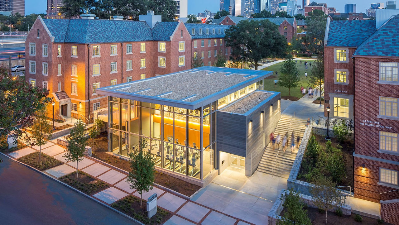 An exterior view of a modern building with illuminated windows and landscaping at dusk