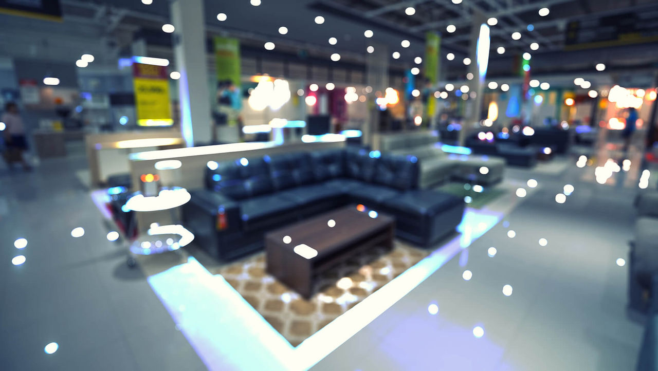View of a furniture store showroom floor seen through a glass window speckled with the reflections of bright lights overhead
