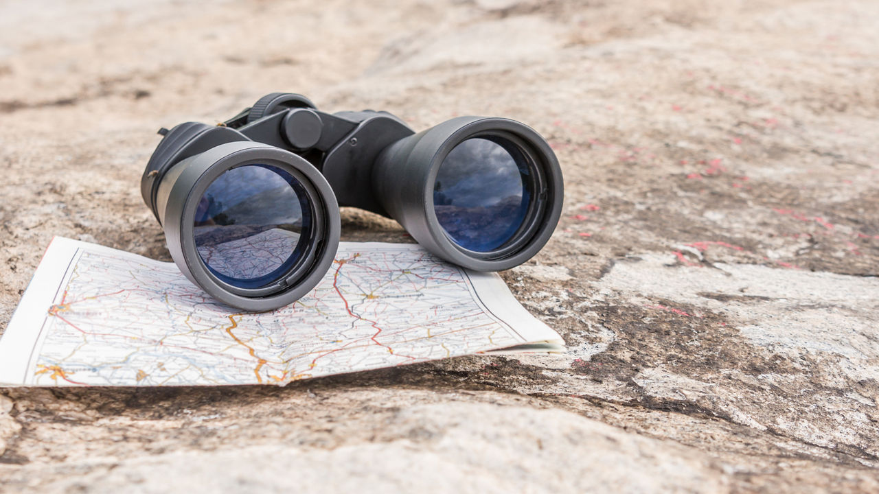 A pair of binoculars on a map, which rests on sandy ground