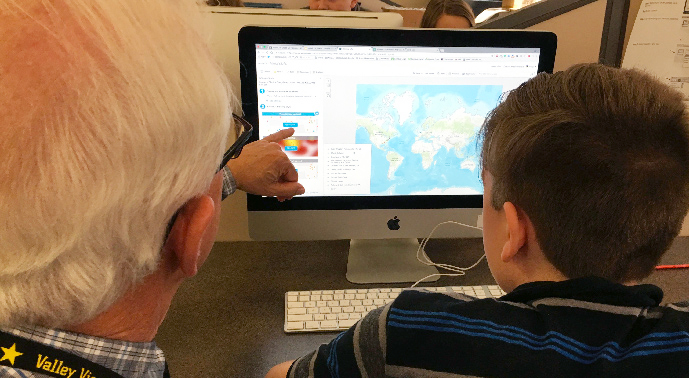 Educator pointing to computer screen with map next to student.