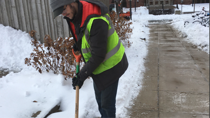A UMN staff member shovels snow to a pile on left