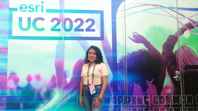Diana stands in front of a blue and purple wall graphic with the UC 2022 logo