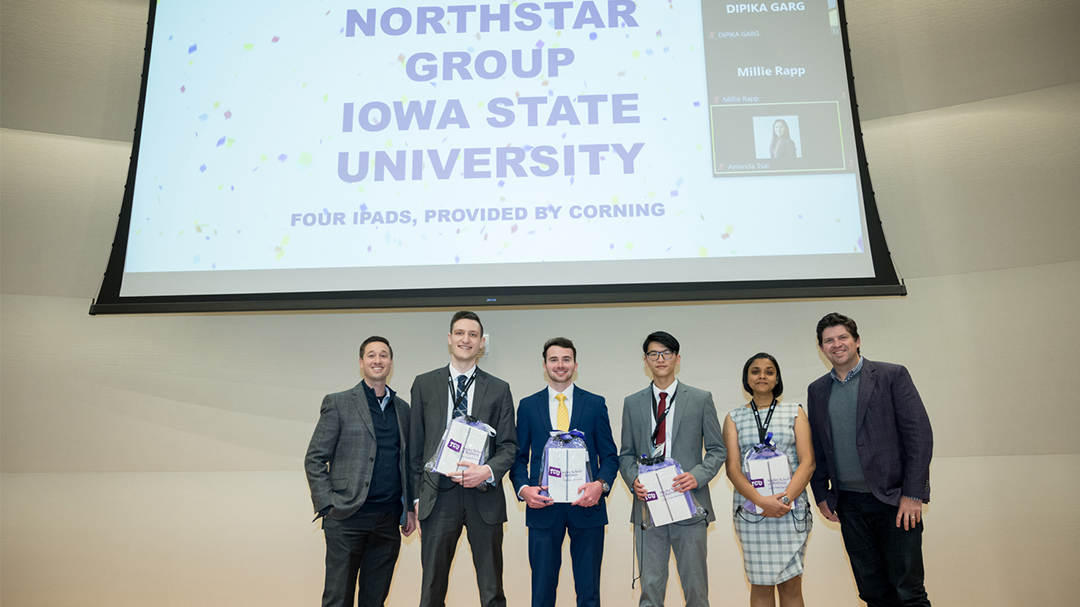 The four first-place winning students pose with their iPads and two team sponsors with a live feed displayed with participating virtual students
