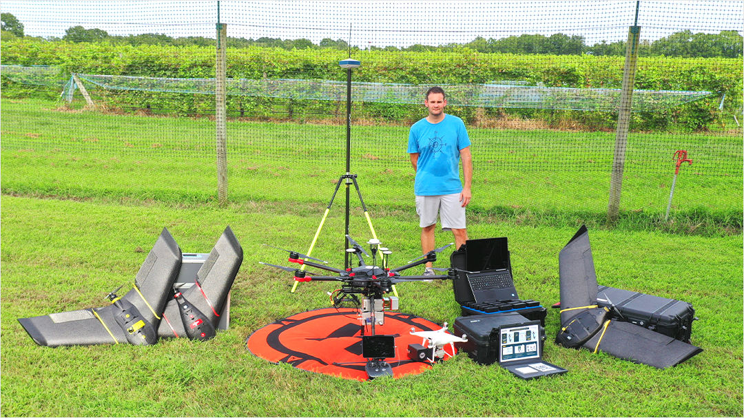 Shuart stands in a field with drone equipment before a class project.