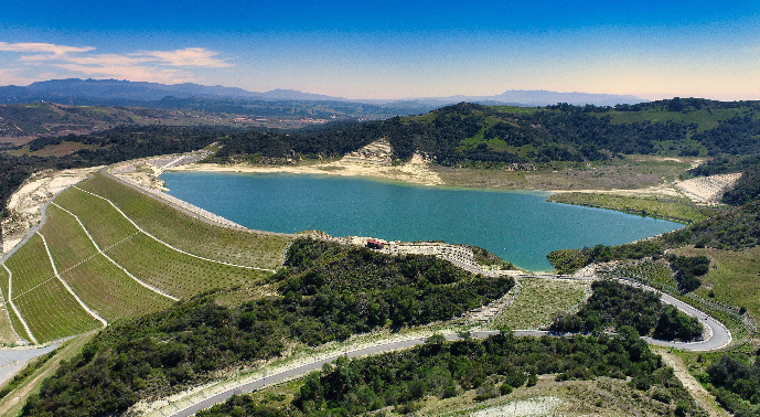 A blue body of water surrounded by green land, trees, and mountains representing the SMWD Trampas Canyon Dam & Reservoir