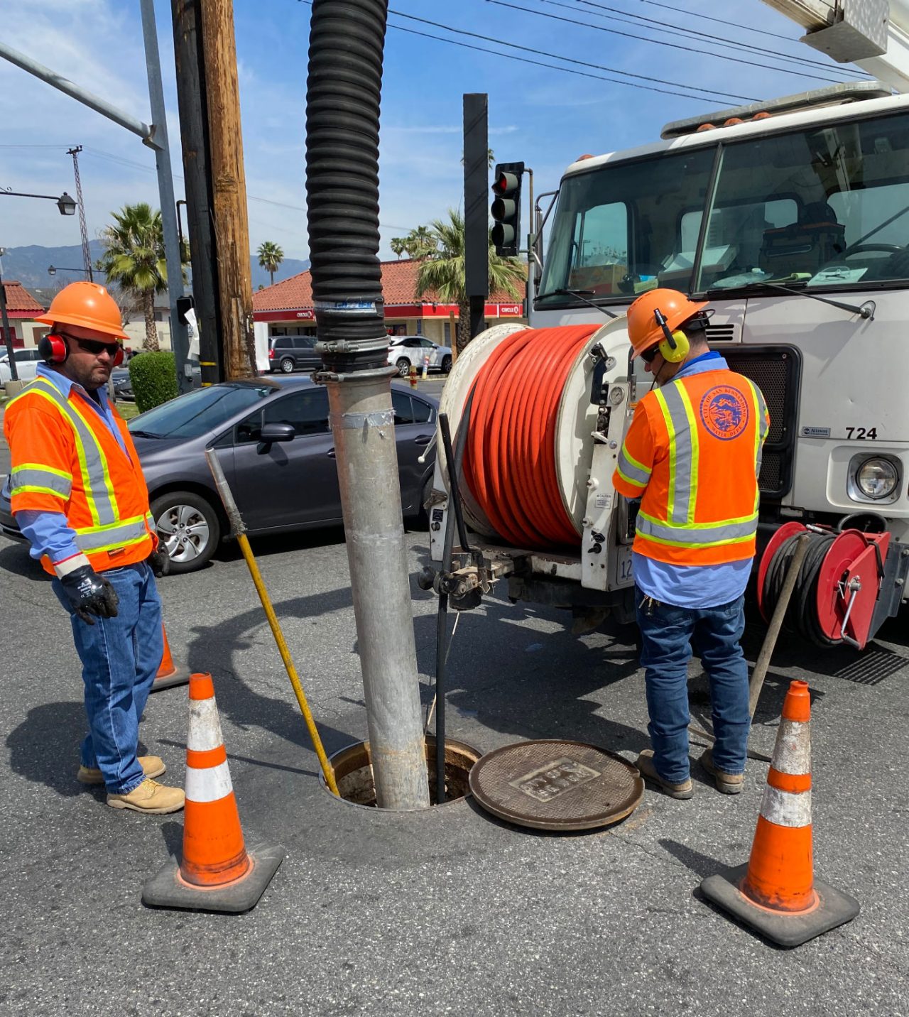 Workers in orange vests working on a manhole in the road