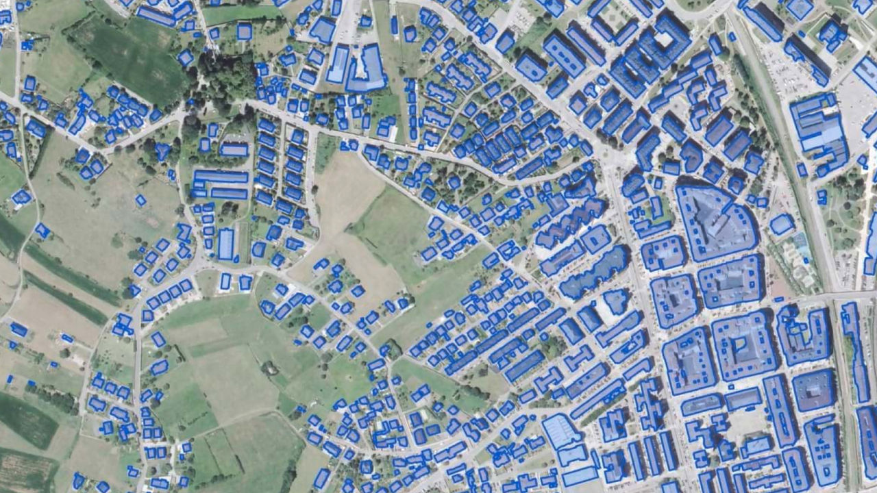 Vue aérienne de quartiers et de terres agricoles avec des bâtiments identifiés et délimités par un modèle d’IA