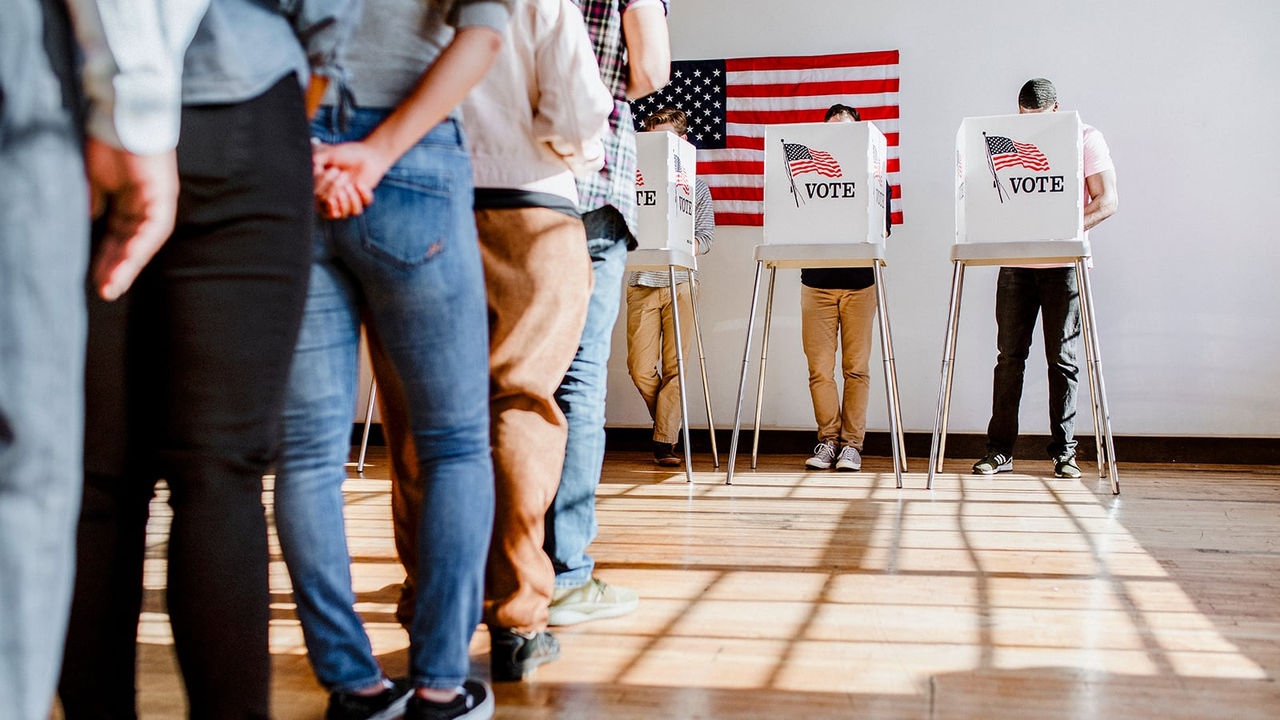 Vue arrière d’une file de personnes en attente de voter dans un bureau de vote
