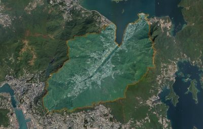 Satellite image of a large wildfire burning in a mountainous region, showing white smoke plumes and an orange burn area