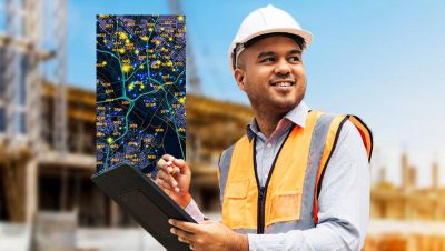 Homme à l’extérieur, près d’un chantier de construction, portant un casque et un gilet de sécurité et tenant une tablette qui affiche une carte détaillée