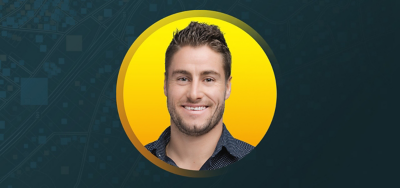 Portrait of Anthony Le Guen smiling in a dark blue patterned shirt with an abstract blue and white background