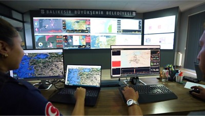 Two people sit in front of computers and video wall displaying maps, charts and data visualizations