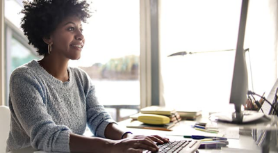 A woman sits at a desk using a laptop in a bright, modern workspace.