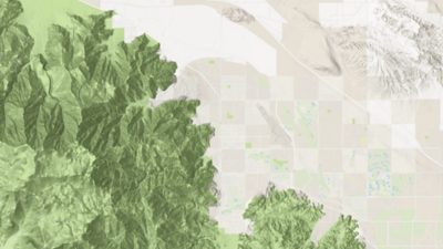 Aerial map of a desert city shown in beige situated between mountain ranges that are colored in green