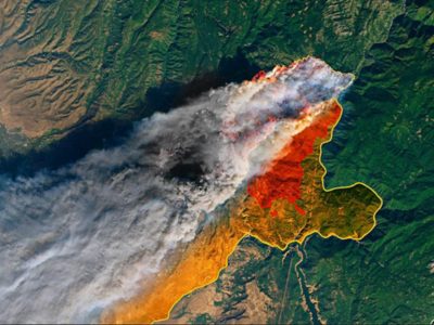 Image satellite d’un grand incendie dans une région montagneuse, montrant des panaches de fumée blanche et une zone brûlée orange