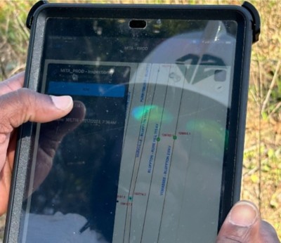 A hand holding a tablet. The tablet displays a map with a blue line and several green dots. The blue line is labeled “Yemassee-Bluffton 230kv.” The green dots are labeled “Bluffton-Rose Hill 115kv,” “Varnville-Bluffton 115kv,” and “Purkysbur-Bluffton.”