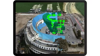 Vue aérienne d’un grand bâtiment incurvé en construction au bord de l’eau, avec des superpositions numériques bleues et vertes indiquant les plans architecturaux.