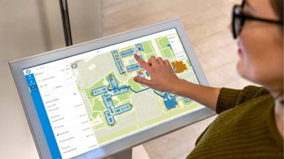 Person using a touch screen monitor displaying a detailed facility floor plan for indoor navigation