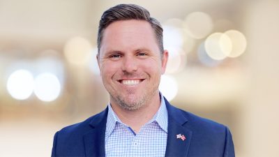 Chris smiling in a business suit standing in a modern office in soft focus